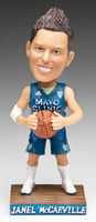 A bobblehead figure on a wood base against a background with a gradient of white to black. The figures wears a basketball jersey and holds a basketball.